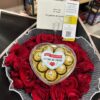 Ramo de rosas rojas con una caja de chocolates Ferrero Rocher en forma de corazón y una tarjeta de regalo personalizada.